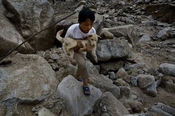 Mao Luojian, 15, from Yueyang, Hunan province, lost his parents and grandparents during a landslide. Carrying his dog, Mao walks through the ruins on June 11. Many netizens on micro blogs responded to media calls to help Mao. Family lost to landslide, boy is left with dog